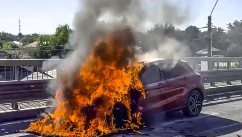 Imagine ilustrativă cu o autospecială de pompieri intervenind lângă un vehicul cuprins de flăcări pe un drum