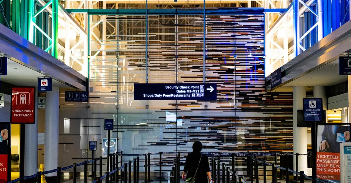 Persoană singulară într-un terminal de aeroport luminat, apropiindu-se de punctul de control de securitate, fără coadă vizibilă.