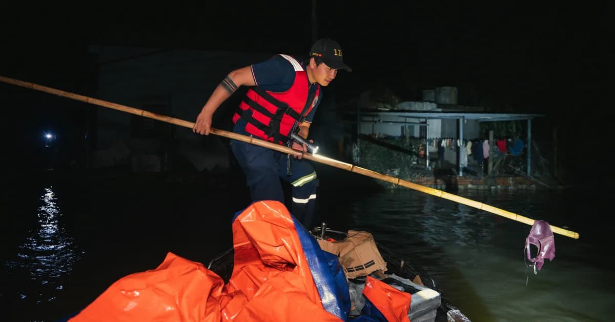 Bărbat în vestă de salvare și șapcă, vâslind o barcă încărcată cu saci portocalii în apă întunecată, noaptea.
