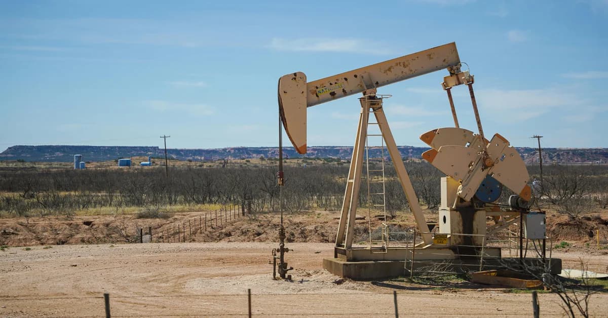 Pompa petrolieră într-un peisaj arid, cu cer senin și structuri industriale în fundal.