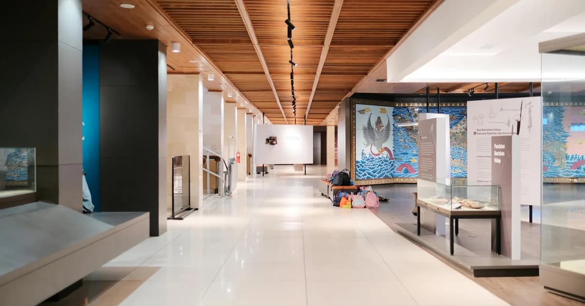 Holul unui muzeu modern, cu exponate amplasate în vitrine de sticlă și decorațiuni murale colorate pe pereți.