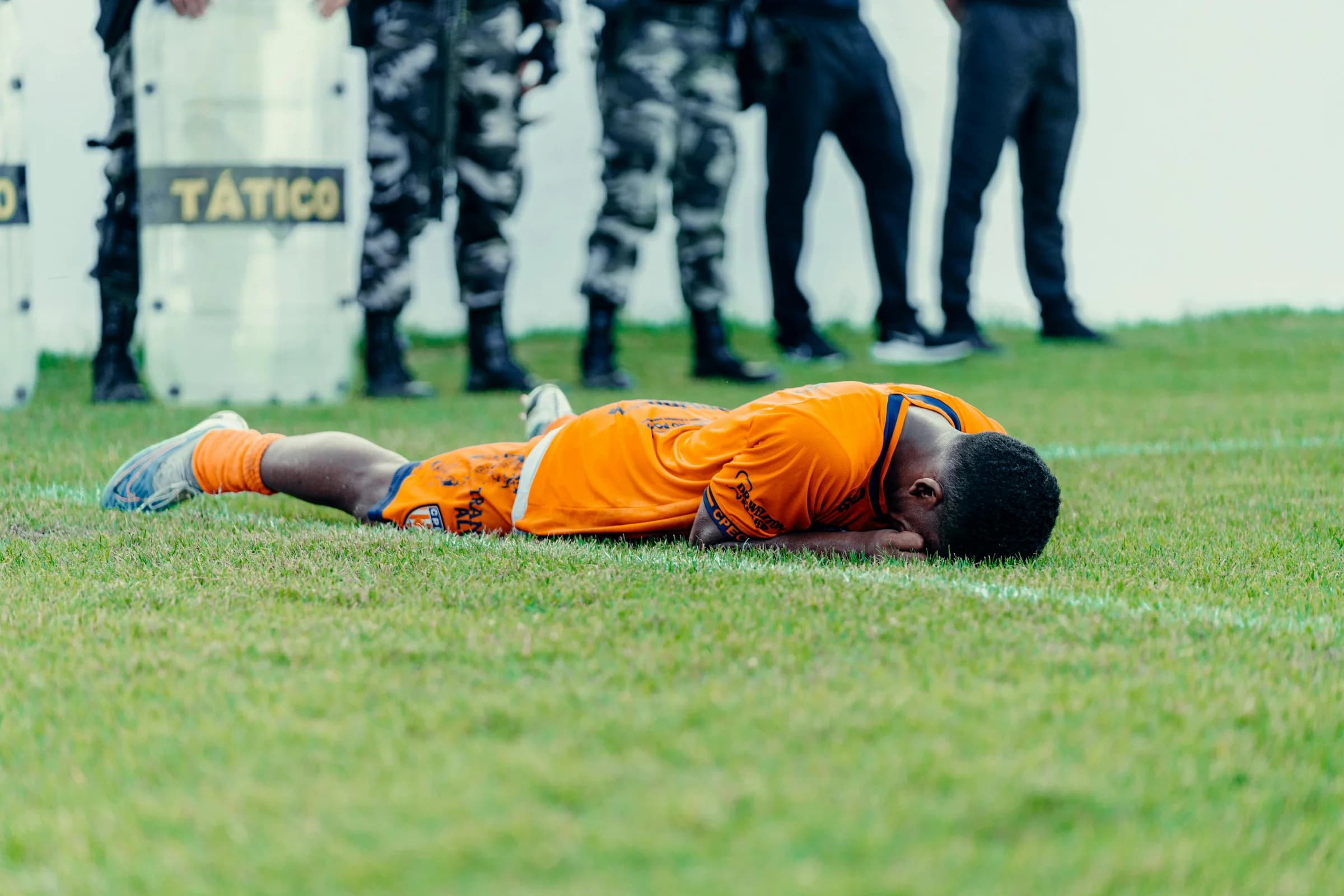 Injured football player in orange jersey lying on field with police presence.