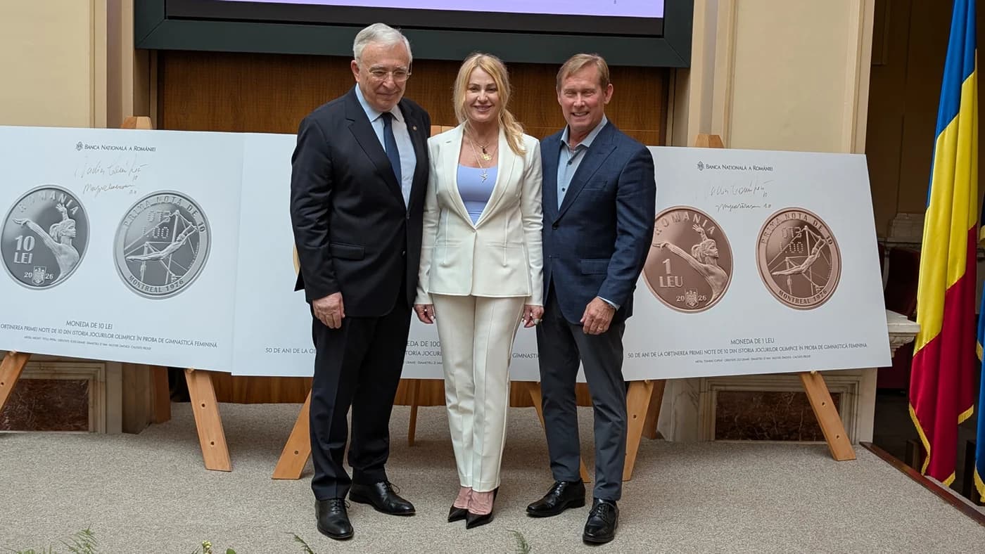 Nadia Comăneci alături de doi bărbați în costum, la un eveniment public, în fața unor afișe cu monede comemorative BNR dedicate primei note de 10 din istoria gimnasticii, Montreal 1976.