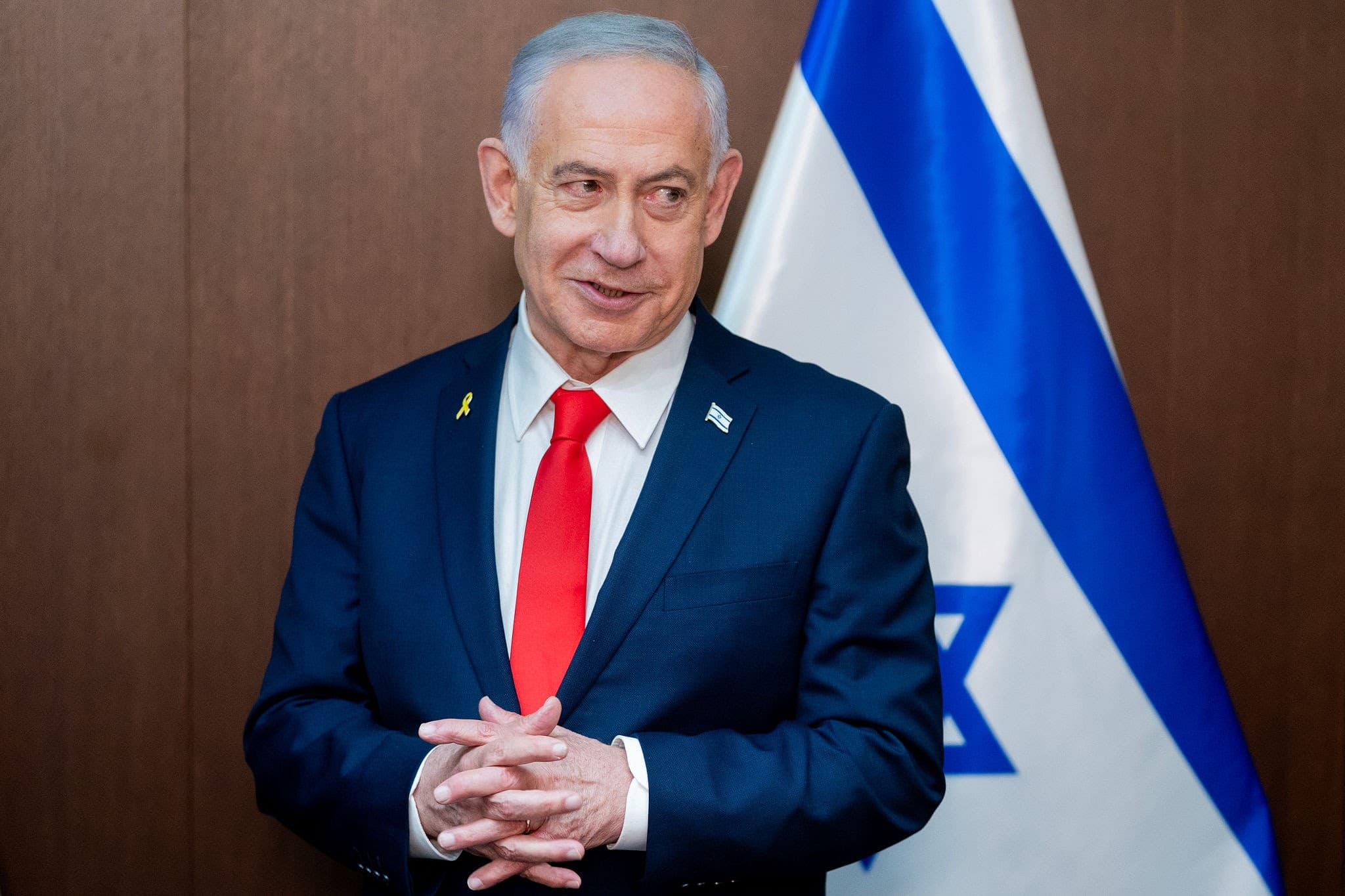 Benjamin Netanyahu, prim-ministrul Israelului, purtând costum oficial bleumarin și cravată roșie, pozând în fața steagului național israelian. (Foto: Pool)